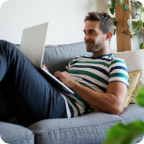 A man lays on a couch and uses a laptop.